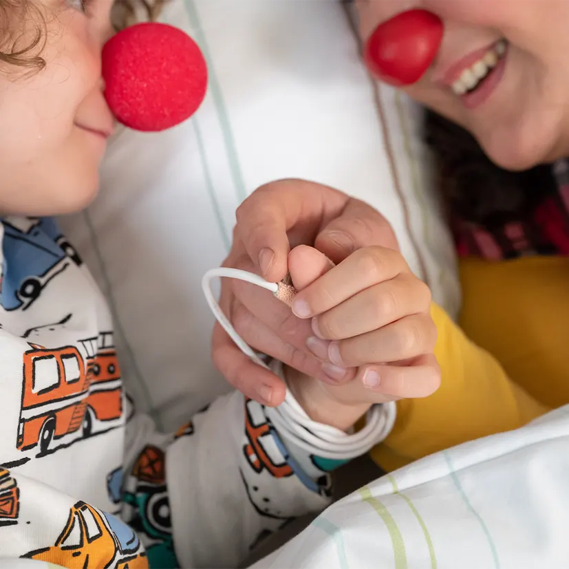 Ein Kind mit roter Clownsnase hält lächelnd die Hand eines Kölner Klinik-Clowns